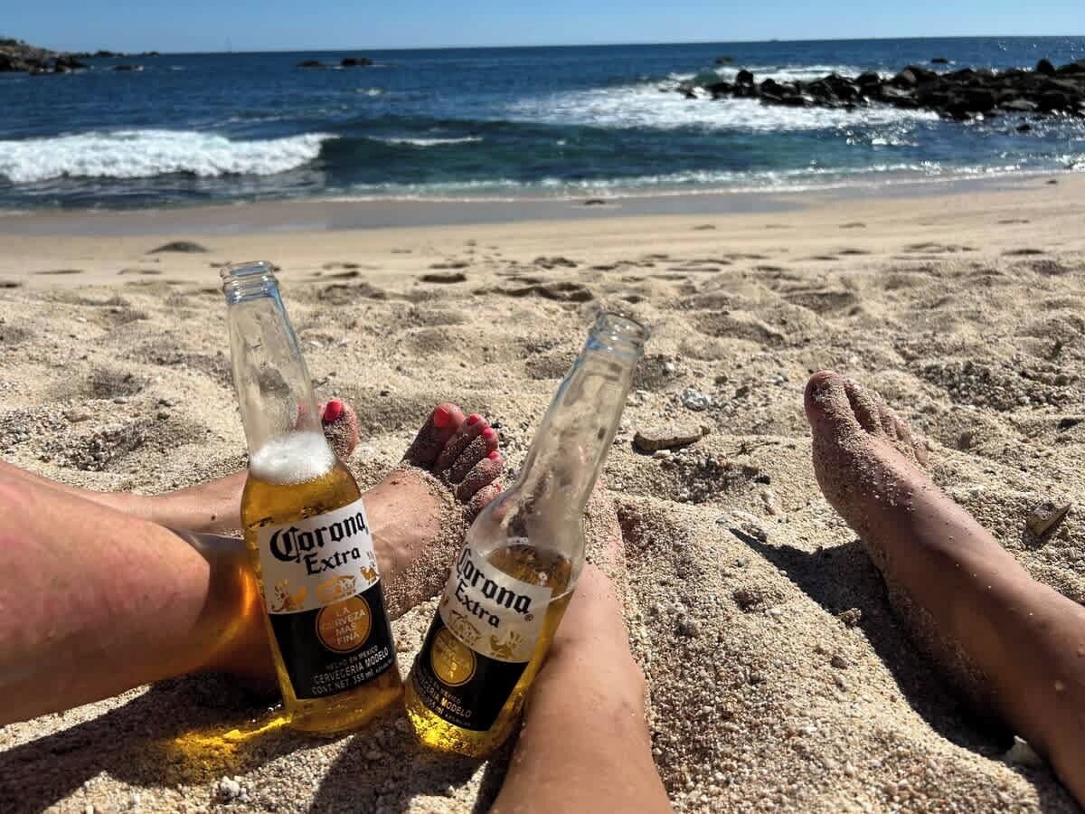 Två flaskor Corona Extra-öl på en sandstrand med havsvågor i bakgrunden.