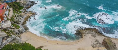A coastal hotel with a beach view, rocky shoreline, and a swimming pool.