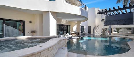 A modern pool area with a hot tub, outdoor seating, and a two-story building with balconies.