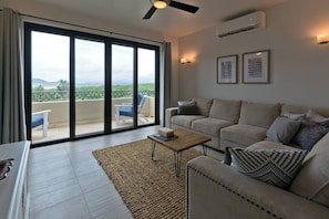 A modern living room with a sofa, coffee table, and a view of a balcony with outdoor furniture. - Marbella Lane Premium Ocean View Villa & Pool (Cabo San Lucas)