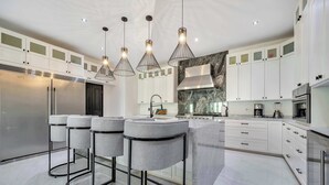 A modern kitchen with white cabinets, a central island, bar stools, and pendant lighting. - Marbella Lane Coastal Elegance Villa with Pool (Cabo San Lucas)