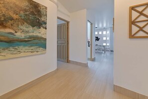 A hallway with a large painting, a wooden door, and a dining area with tables and chairs. - Marbella Lane Coastal Elegance Villa with Pool (Cabo San Lucas)