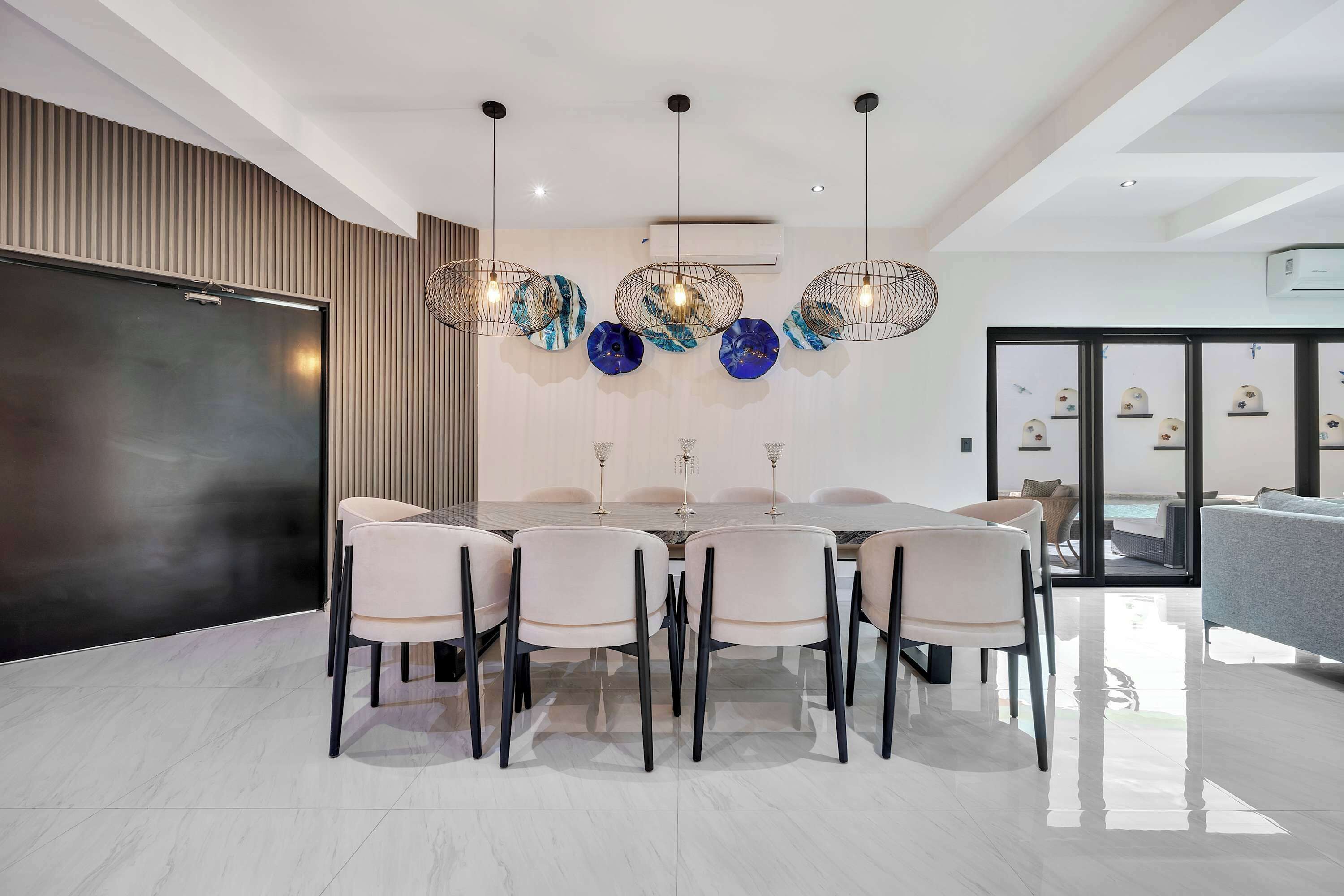 A modern dining area with a round table, six chairs, and a unique pendant light fixture.