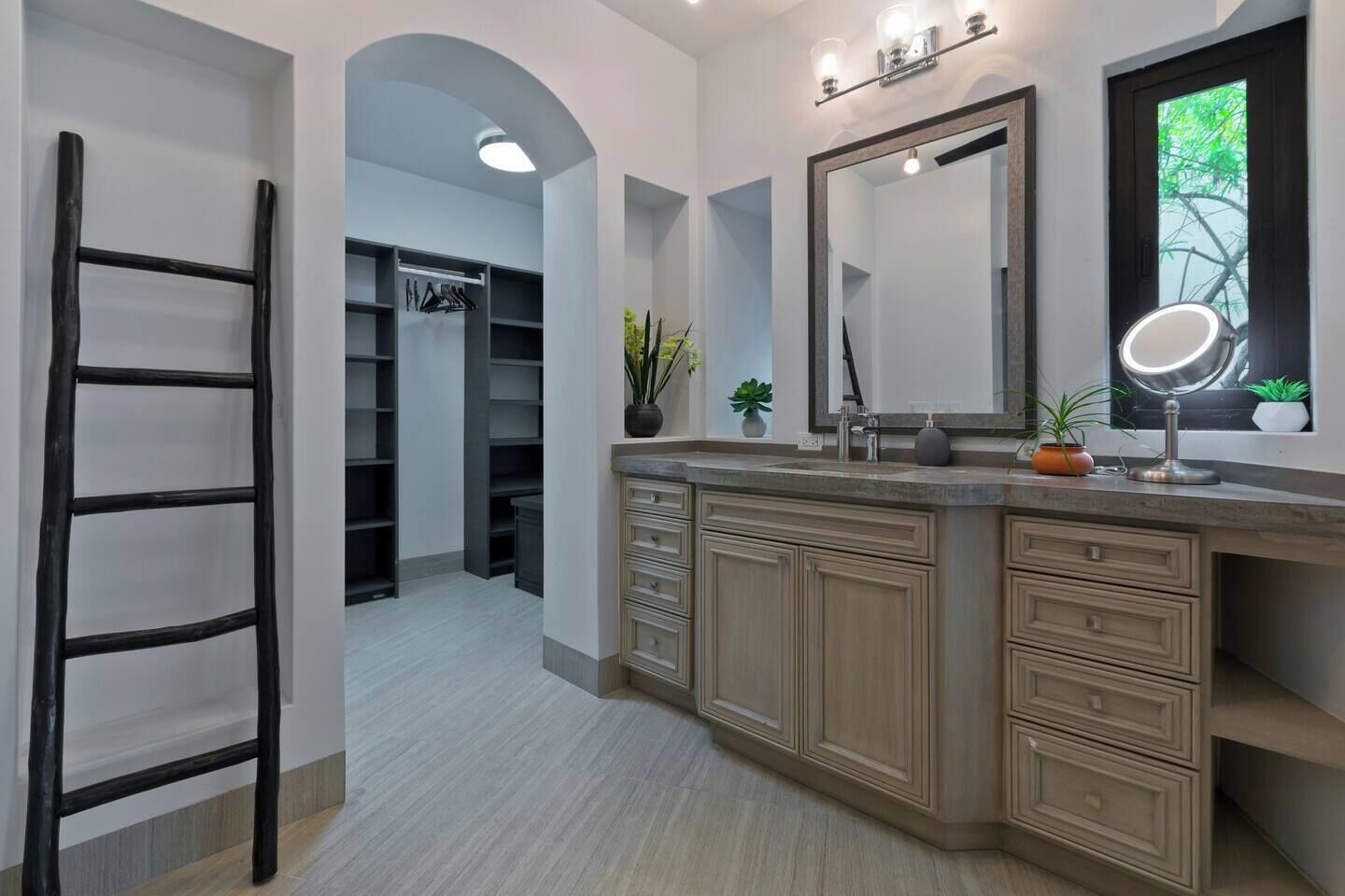 A modern bathroom with a large vanity, a mirror, and a window with a view of greenery.