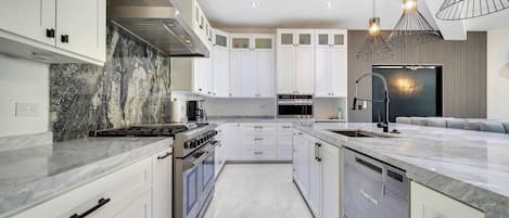 A modern kitchen with white cabinetry, stainless steel appliances, and a marble countertop.