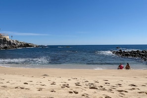 Ein Strand mit Fußspuren, die zum Wasser führen, eine felsige Küstenlinie und ein klarer Himmel.