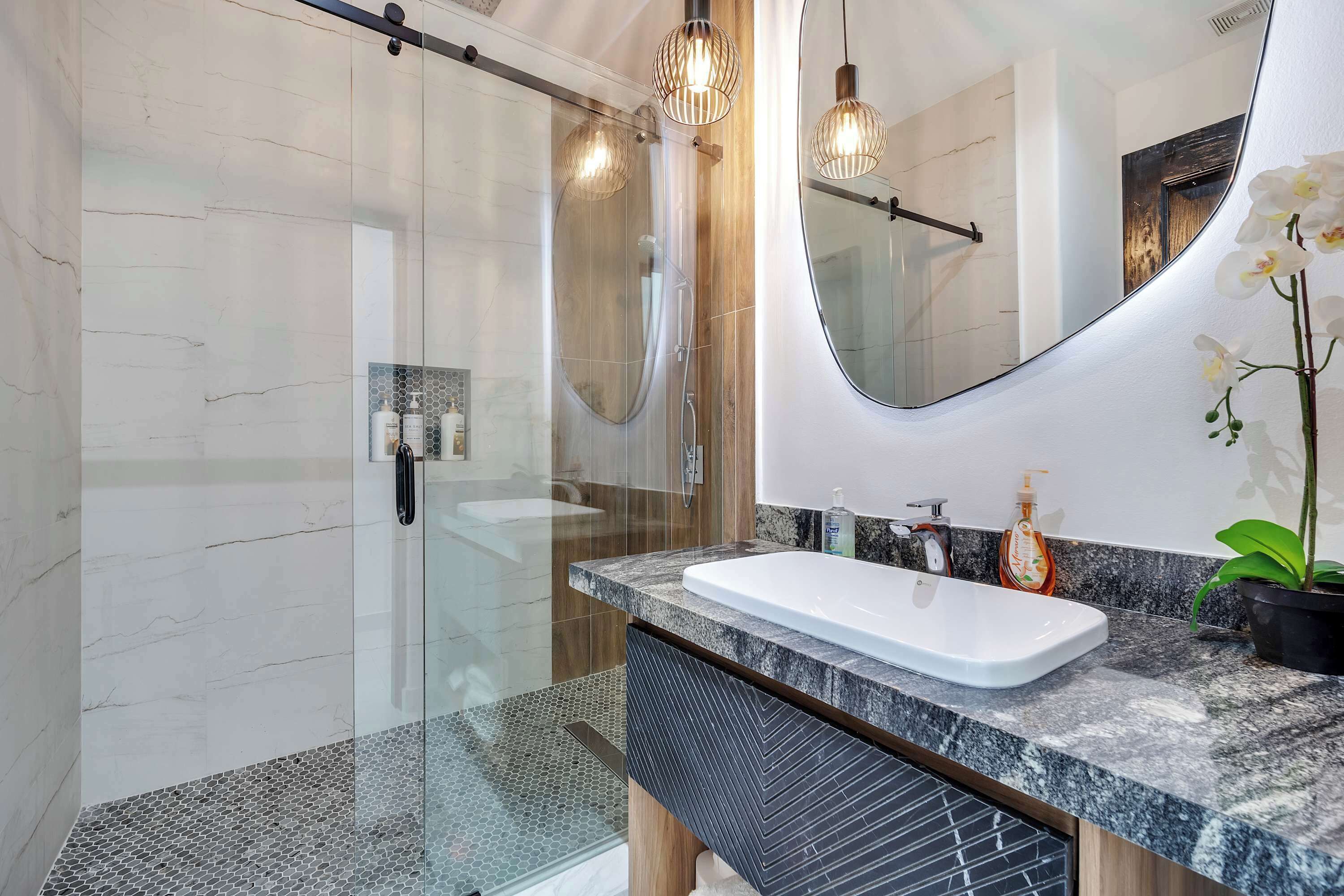 Une salle de bain moderne avec une douche à parois de verre, un grand miroir et un plan de toilette en marbre.