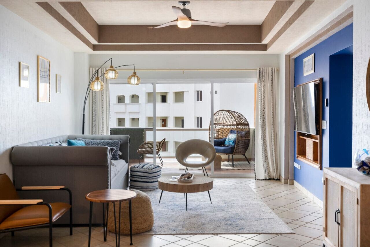 A modern living room with a sofa, chairs, a coffee table, and a balcony with a view of a building.