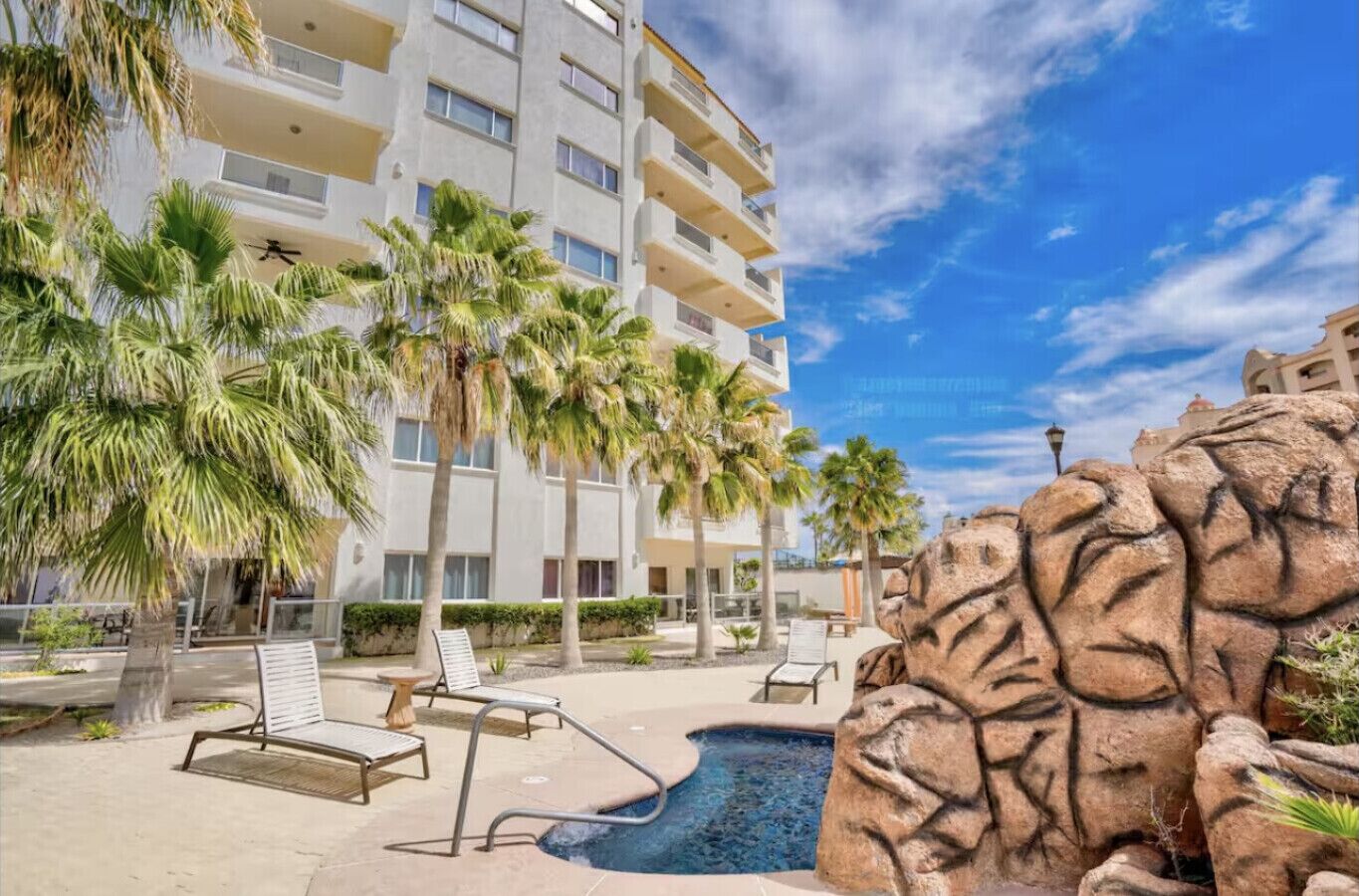 A hotel with a pool area, palm trees, and a rocky feature.