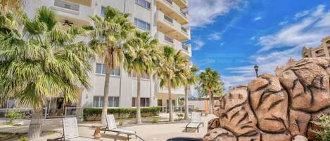 A hotel with a pool area, palm trees, and a rocky feature.