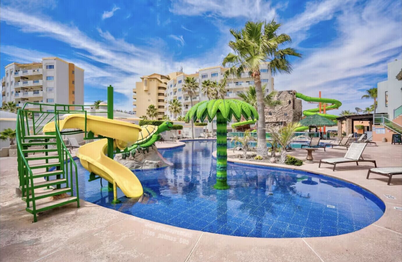 A swimming pool with slides and palm trees, surrounded by buildings.