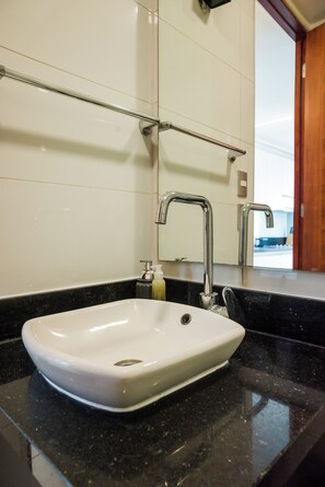 A bathroom with a white sink, a mirror, and a black countertop. - Charming Studio in Las Condes  (Las Condes)