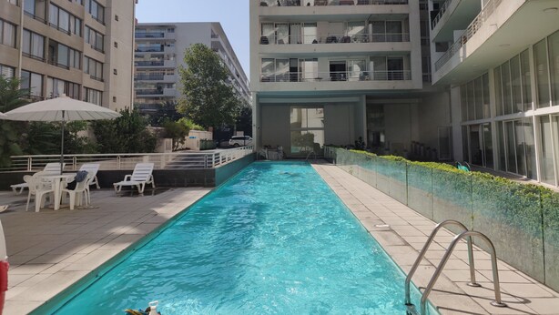 A swimming pool with lounge chairs and umbrellas, surrounded by high-rise buildings. - Charming Studio in Las Condes  (Las Condes)