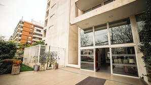 A modern building with a glass entrance, a gated area with potted plants, and a paved walkway. - Charming Studio in Las Condes  (Las Condes)
