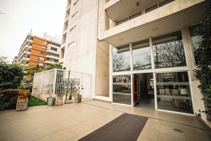 A modern building with a glass entrance, a gated area with potted plants, and a paved walkway. - Charming Studio in Las Condes  (Las Condes)