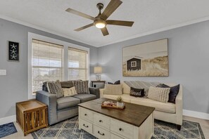 Uma sala de estar com ventilador de teto, dois sofás, uma mesa de centro e uma mesa lateral.