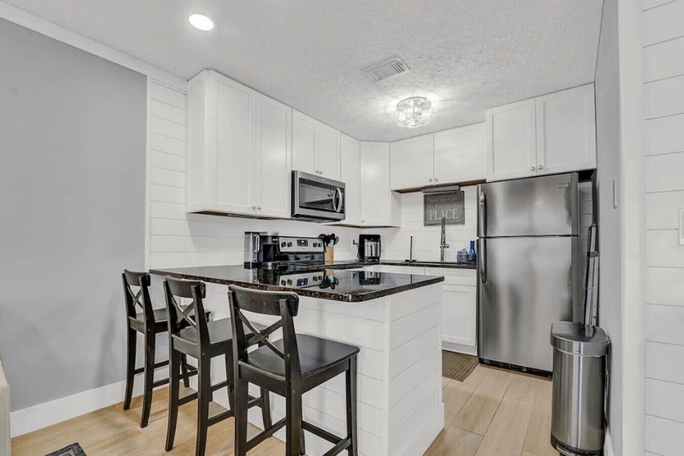 A modern kitchen with white cabinetry, a stainless steel refrigerator, a microwave, and a coffee maker.