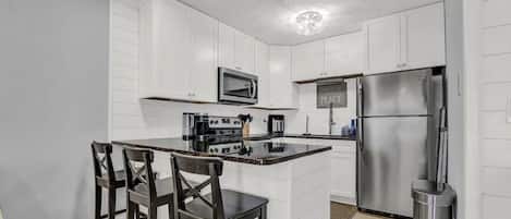 A modern kitchen with white cabinetry, a stainless steel refrigerator, a microwave, and a coffee maker.