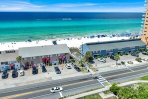 Ein Küstenhotel mit Parkplatz, einer Straße mit Fahrzeugen und einem Strand im Hintergrund.
