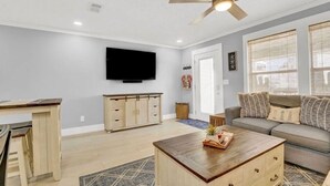 Una sala de estar con ventilador de techo, televisor montado en la pared, sofá, mesa de centro y mueble.