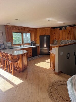 A kitchen with wooden cabinets, a refrigerator, a coffee maker, and a large window. - Superb White Sand Lake home in charming Baxter with beautiful white sand beach. (Baxter)