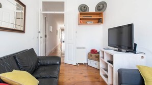 Un soggiorno con un divano in pelle nera, una televisione su un mobile bianco e un armadietto in legno con oggetti decorativi.