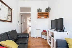 A living room with a black leather sofa, a television on a white stand, and a wooden cabinet with decorative items. - Gulbenkian Park Residence Apartment (Lisbon)