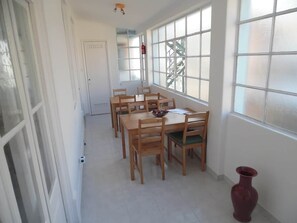 A dining area with a long table and chairs, large windows, and a red vase on the floor. - Gulbenkian Park Residence Apartment (Lisbon)