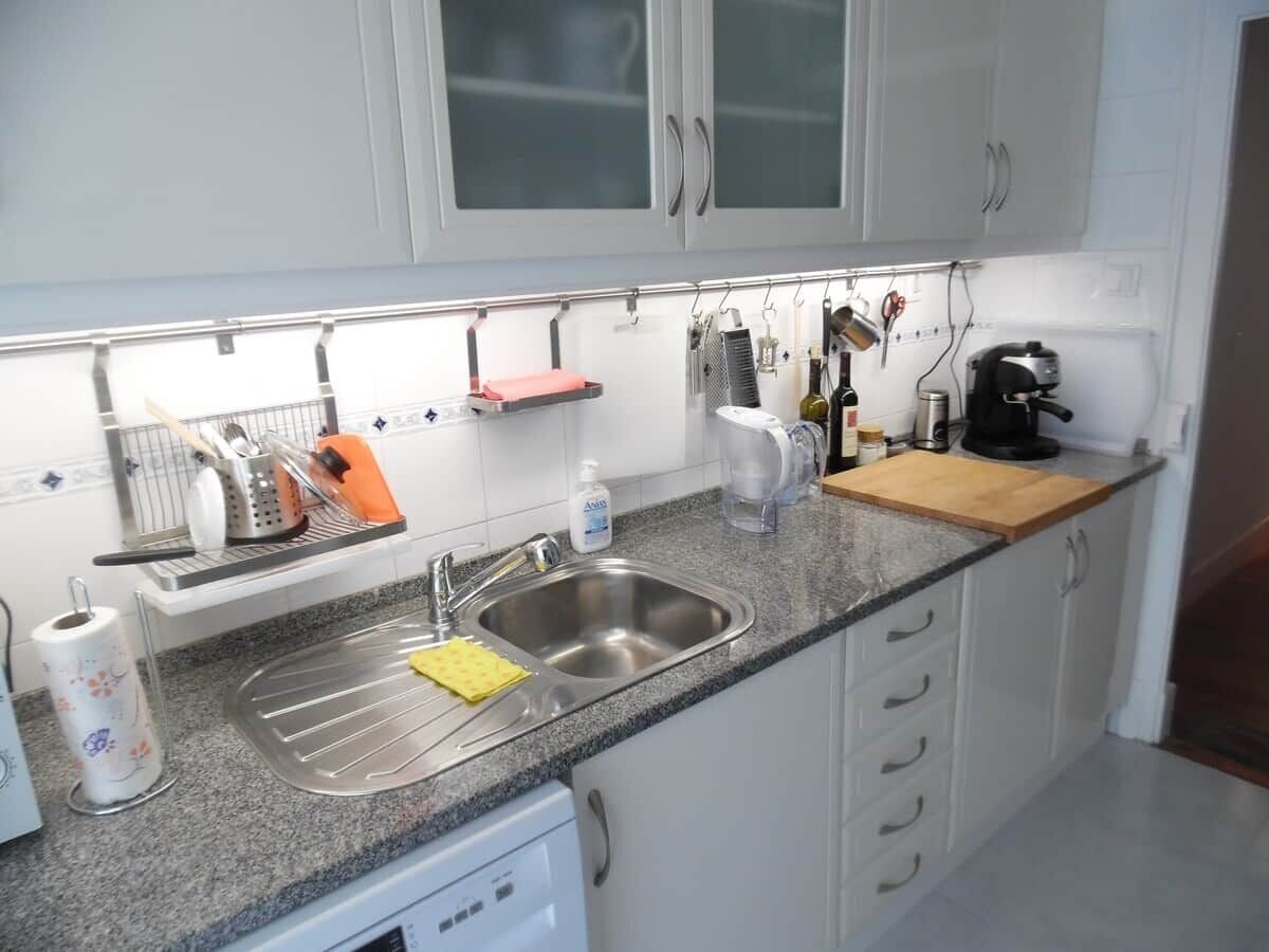 A kitchen with a stainless steel sink, white cabinets, and various kitchen utensils and appliances.
