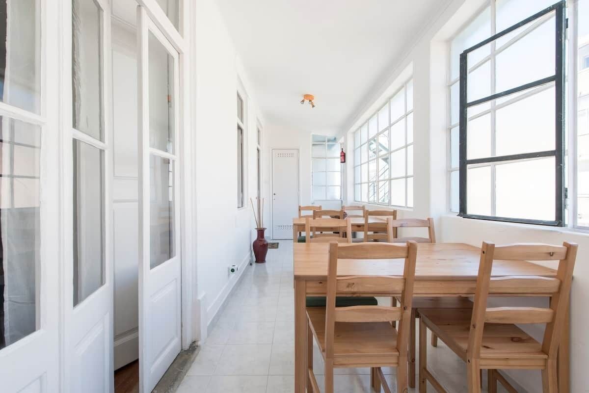 A corridor with a dining table and chairs, white doors, and large windows.