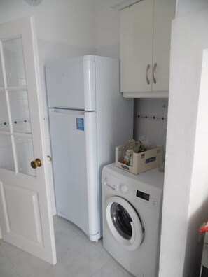 A compact kitchen with a refrigerator, a washing machine, and a cabinet with a microwave. - Gulbenkian Park Residence Apartment (Lisbon)