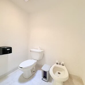 A small bathroom with a toilet, bidet, and a soap dispenser on the wall.