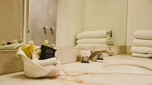 A bathroom with a marble sink, a towel rack with folded towels, and a bottle of soap in a towel.