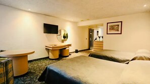 Hotelkamer met twee bedden, een bureau, een spiegel, een televisie en een ingelijst schilderij aan de muur.