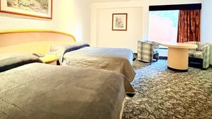 A hotel room with two beds, a small table, a chair, and a window with curtains.