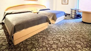 A hotel room with two beds, a small table, a chair, and two framed pictures on the wall.