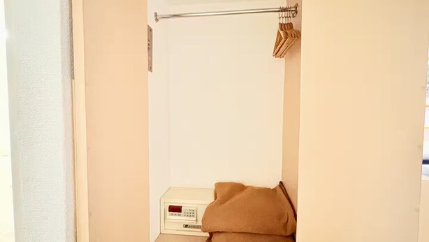 A closet with a hanging rod, a folded item on a shelf, and a box with a remote control.