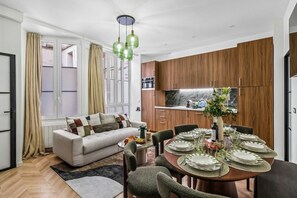 A modern living room with a sofa, dining table set for four, and a kitchen area with wooden cabinets and a marble countertop. - Lavie Maison • Spa Bath & AC in the Heart of Paris (Paris)