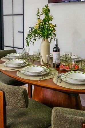 Mesa lista para comer, con platos, copas y una botella de vino, rodeada de sillas.