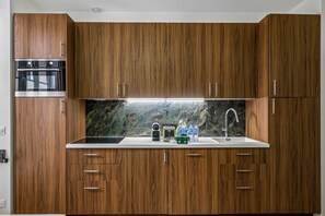 Una cocina con armarios de madera, horno empotrado, salpicadero de mármol, pileta de acero inoxidable y grifo.