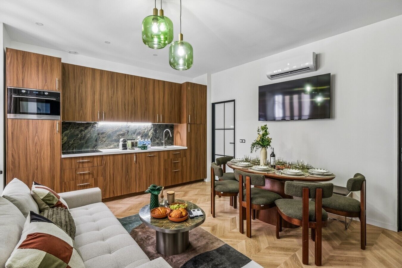 A modern kitchen with wooden cabinets, a built-in oven, and a dining area with a round table and chairs.