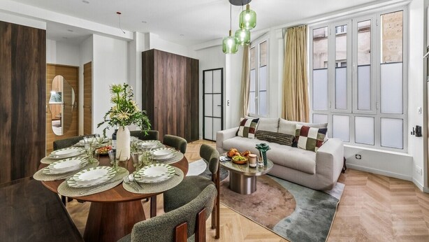 Ein modernes Wohnzimmer mit einer Couch, einem Esstisch für vier Personen und einem großen Fenster mit Vorhängen.