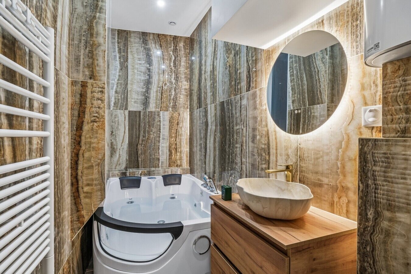 Ein Badezimmer mit Marmorwand, einem runden Spiegel, einem Holzwaschtisch und einer Badewanne.