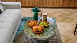 Ein runder Couchtisch mit Tischplatte im Blattmuster, zwei Croissants, eine Schüssel mit Trauben, eine grüne Vase und ein Kerzenhalter.