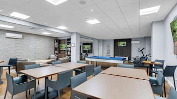 Un espacio interior moderno con mesa de billar, zona de estar y equipo de ejercicio.