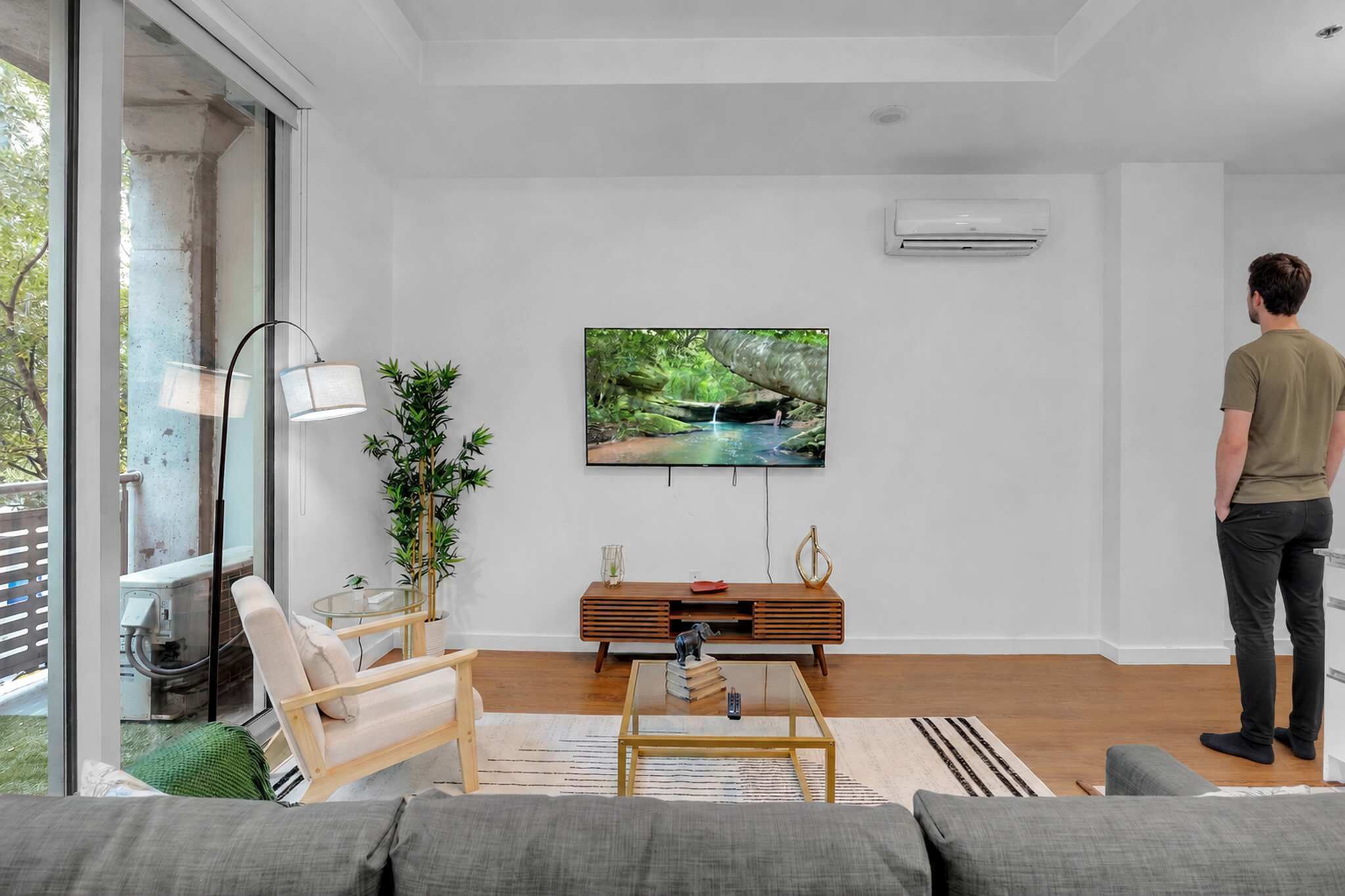 A modern living room with a television, sofa, coffee table, and a person standing.