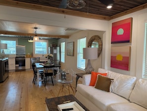 A modern kitchen with a dining area, wooden floors, and a white sofa with decorative pillows. - Cozy renovated 2-bedroom/1 bath cottage only 1 block from the beach! (Folly Beach)