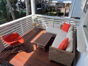 A wooden deck with a wicker sofa, a rocking chair, and a small table. - Cottage beside Bert's in the Heart of Folly Beach-one block to the beach & pier! (Folly Beach)