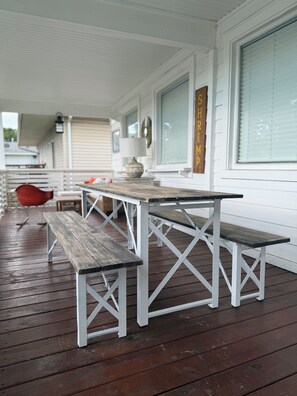 Eine Holzterrasse mit einem weißen Metalltisch und Bänken, einem roten Stuhl und einer Lampe.