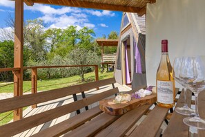 Um deck de madeira com um banco, uma garrafa de vinho e um copo sobre uma mesa.